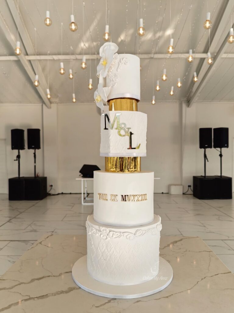 Tall white wedding cake with gold tiers and M&L monogram